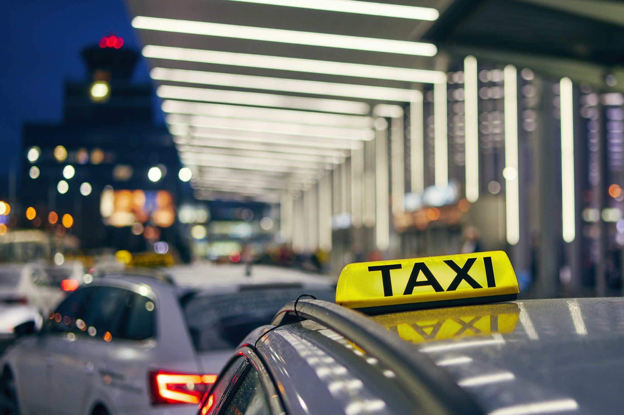 Lighting taxi sign on the roof of car against airport terminal at night. Prague, Czech Republic